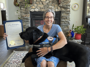 Woman seating with her service dog holding a proclamation